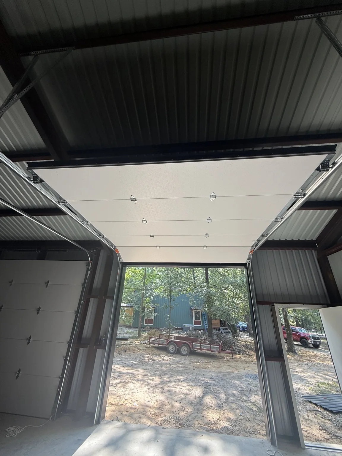 Insulated overhead door with commercial track hardware inside a red iron metal building